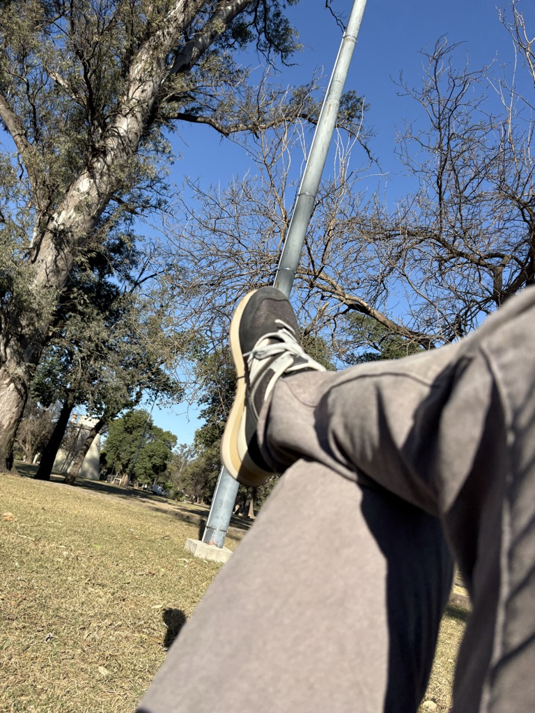 Una persona se sienta en un parque, con la pierna cruzada y un zapato promine...