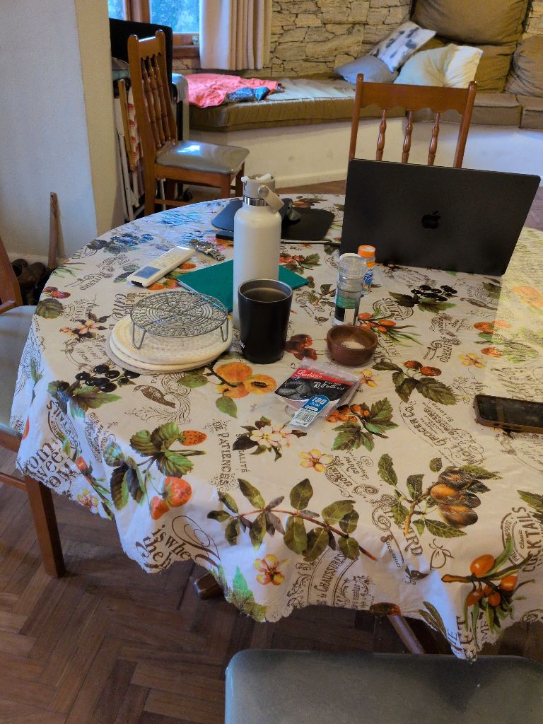 The photo shows a round table in a casual home setting. Various items are sca...