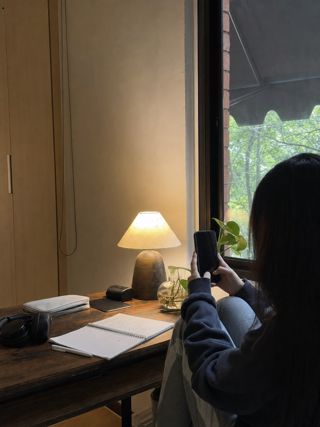 A person is sitting at a wooden desk, looking at their phone. There is a warm...