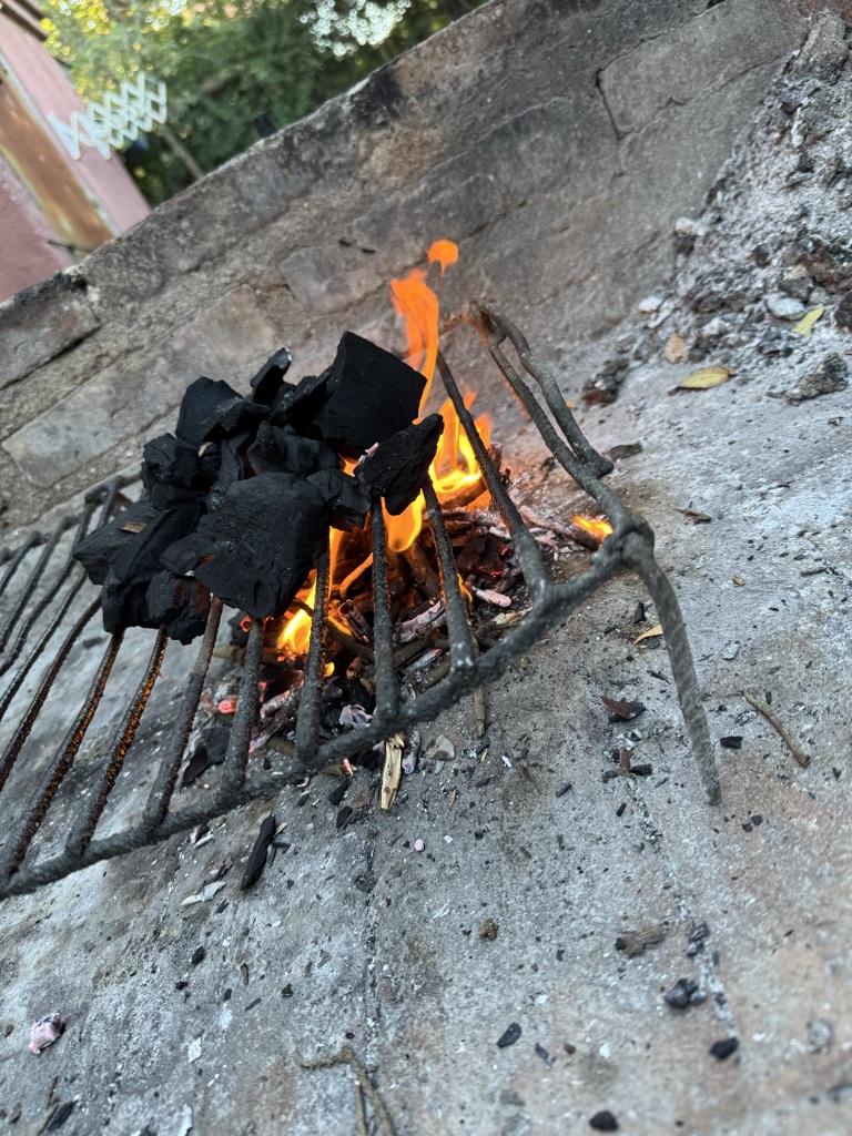 En la imagen, hay un asador con carbón encendido. Las llamas son visibles ent...