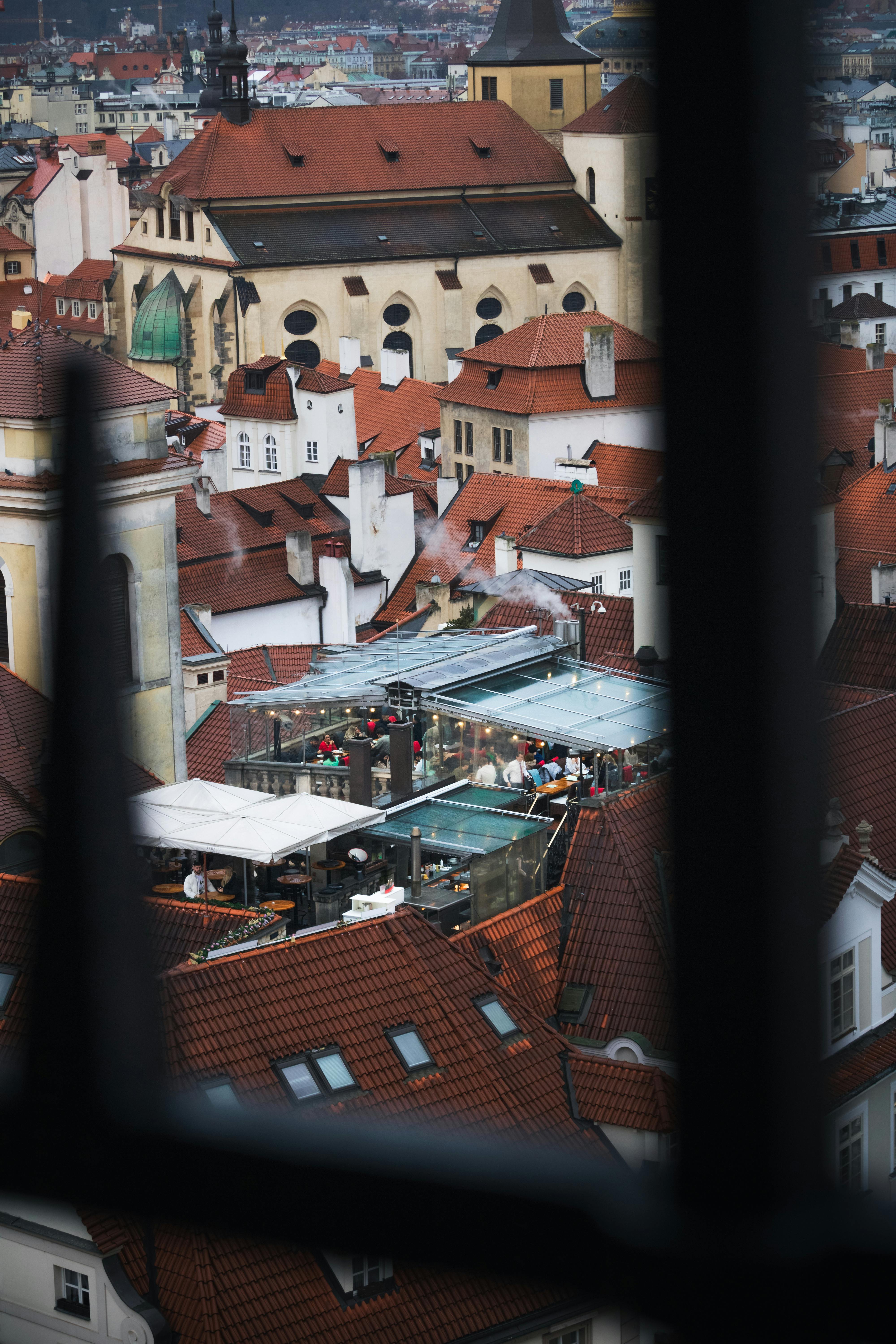 The photo shows a view of a city with many rooftops. There is a restaurant wi...
