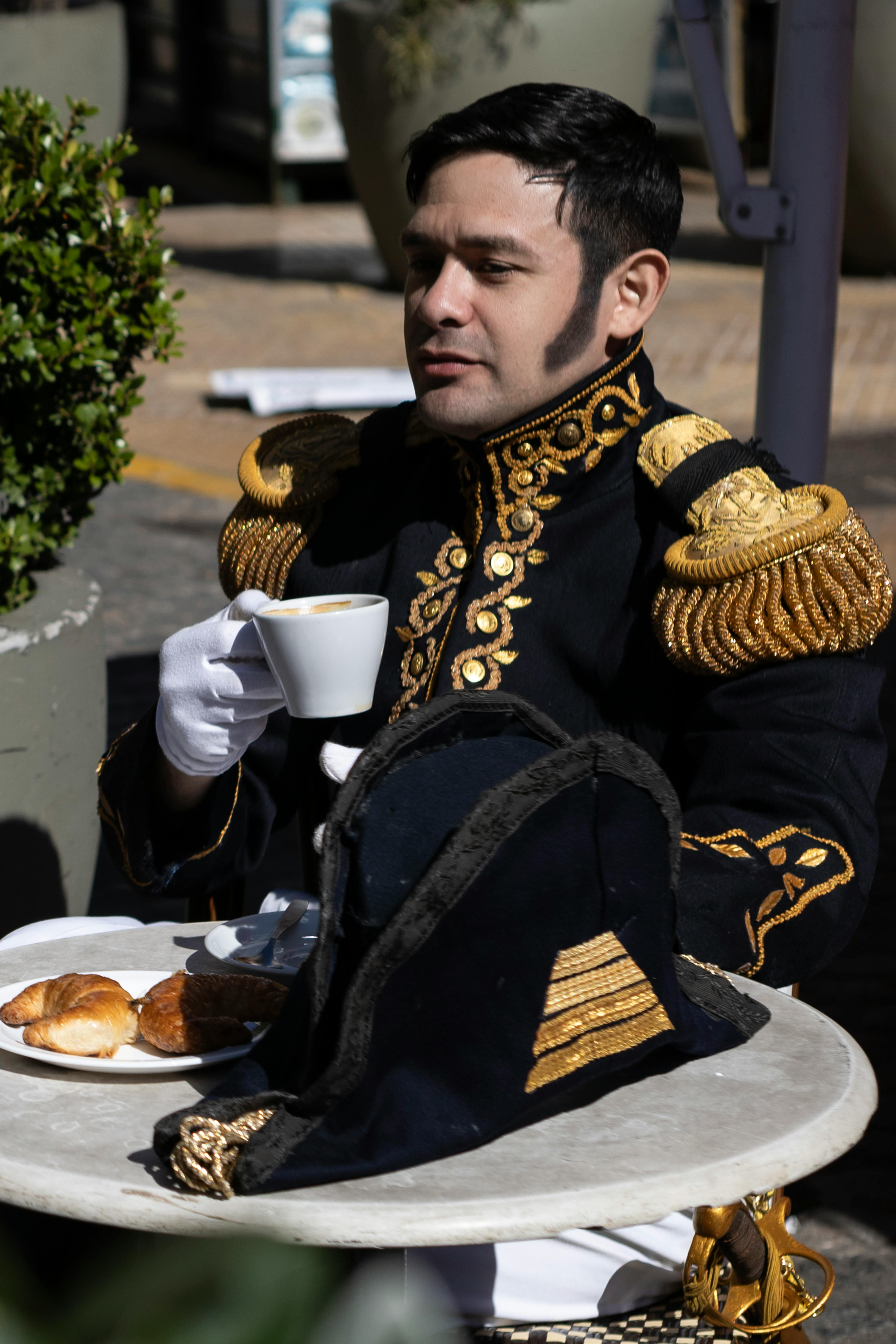 A man in a military-style uniform sits at a table, enjoying a cup of coffee....