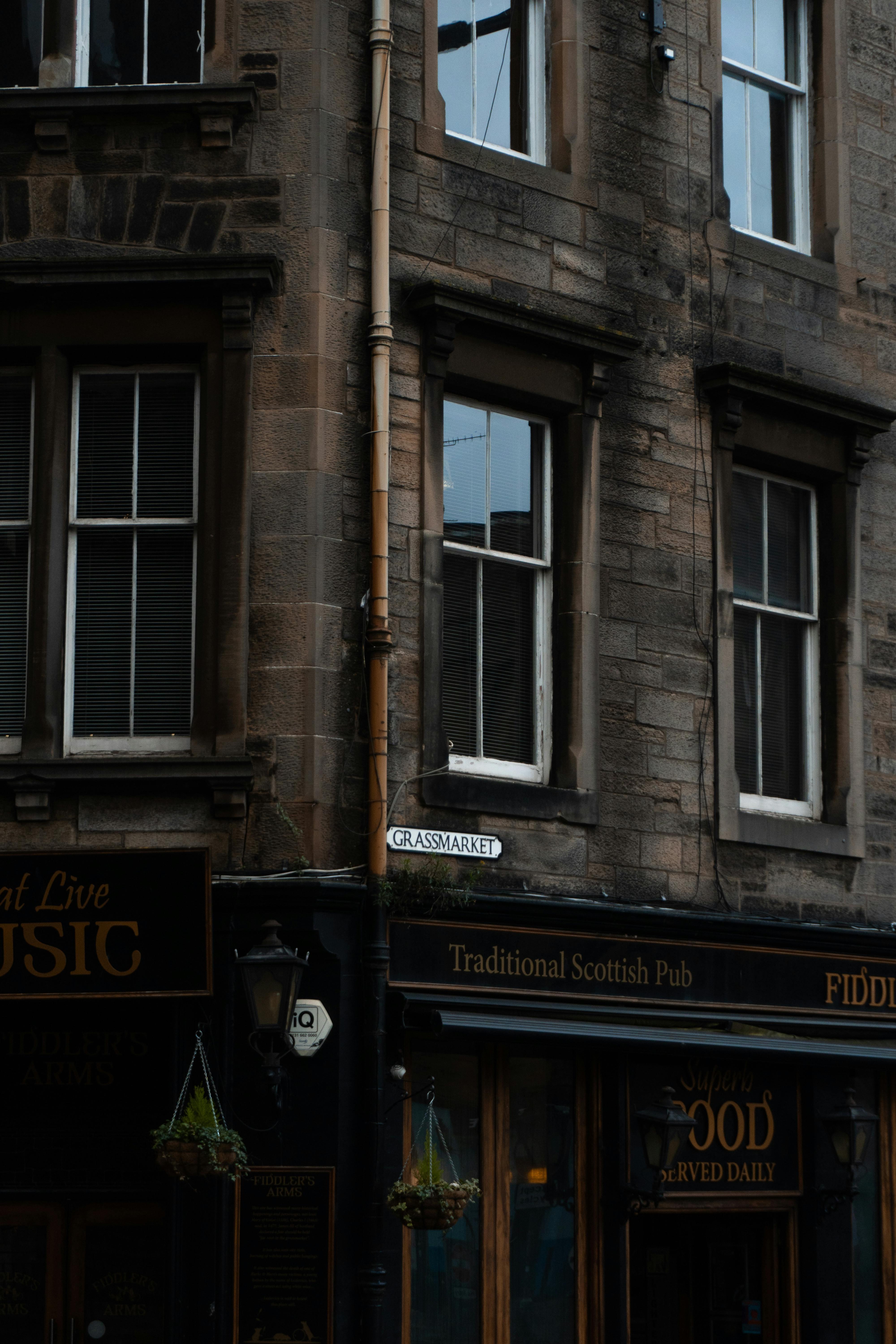 The photo shows a corner of a street with a traditional Scottish pub. The bui...