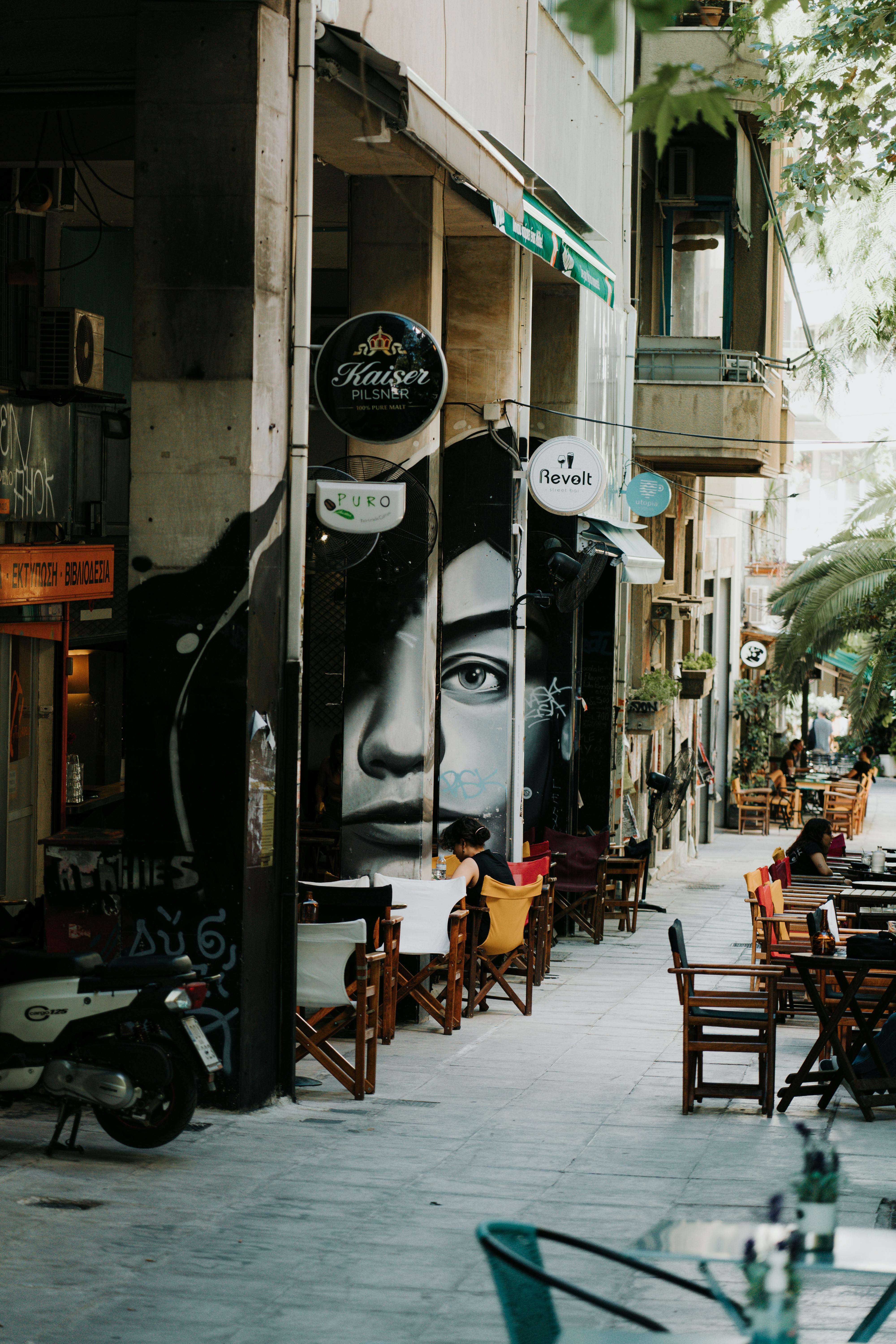 The photo shows a lively street scene with cafes and street art. A large mura...
