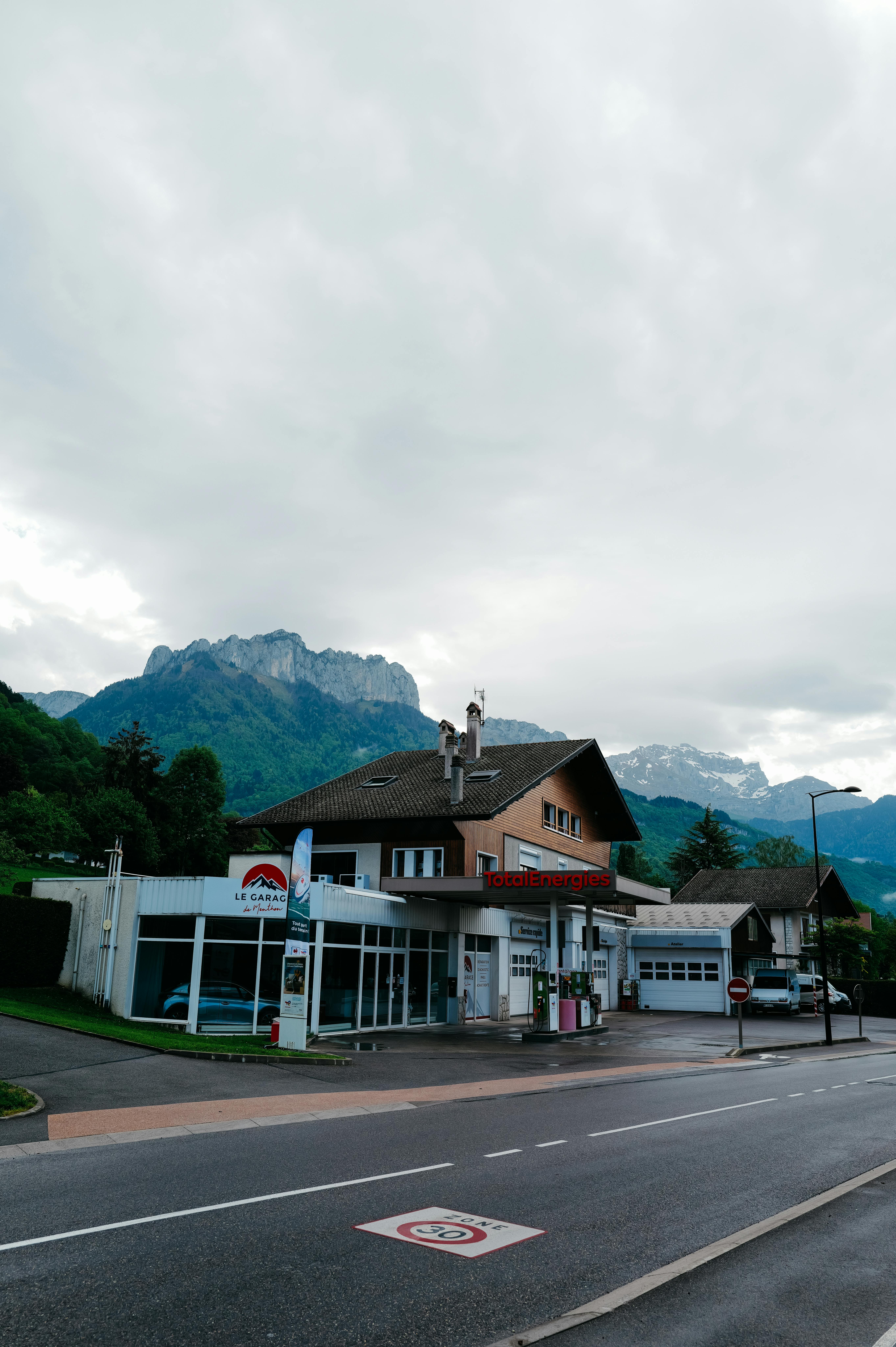 The image shows a gas station with a wooden building in front of tall mountai...