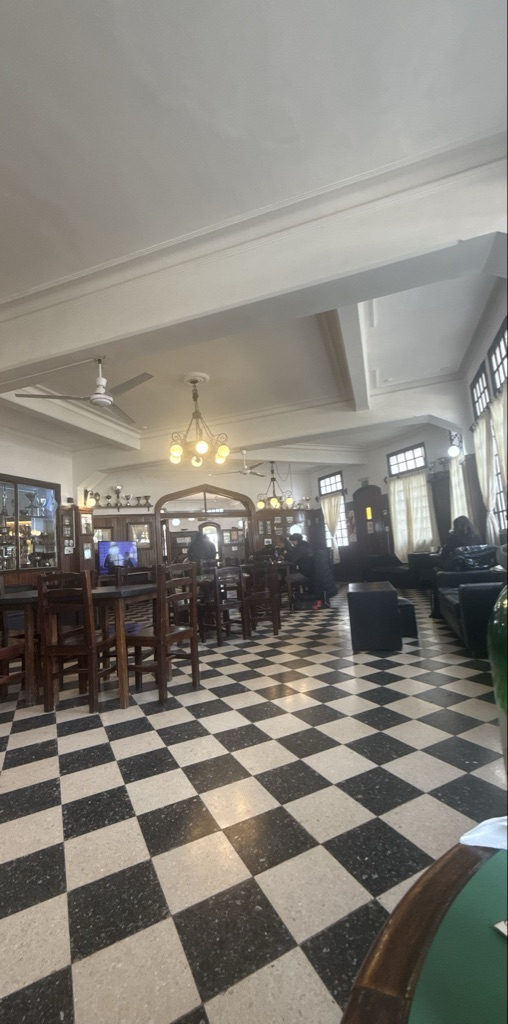 El interior de un restaurante muestra mesas y sillas de madera. Hay luces col...